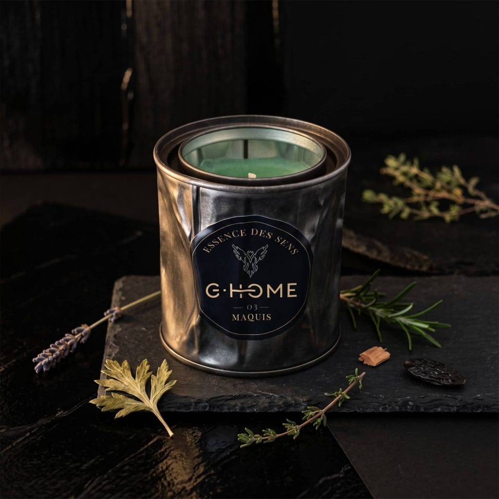 Bougie artisanale Maquis entourée de lavande, thym, romarin, cèdre et fève tonka, illustrant les notes aromatiques de la collection Essence des Sens de G-HOME.