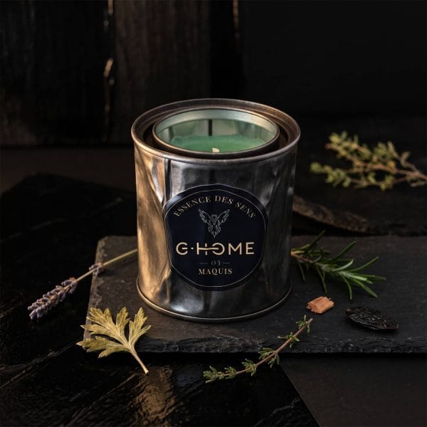 Bougie artisanale Maquis entourée de lavande, thym, romarin, cèdre et fève tonka, illustrant les notes aromatiques de la collection Essence des Sens de G-HOME.